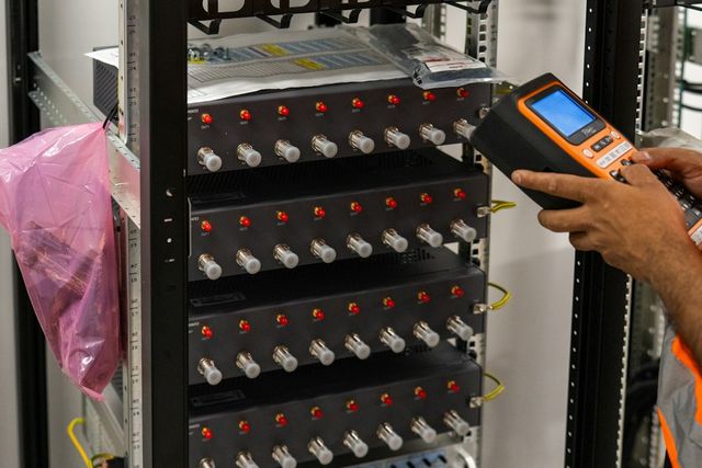 Technician testing connections in a fibre rack with a handheld meter