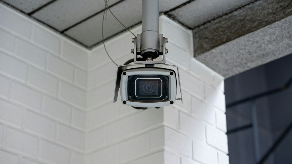 Security camera on a ceiling bracket in the corner of a white brick wall