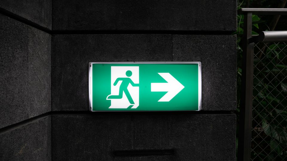 Lit green emergency exit sign on a dark stone wall